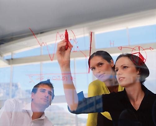 Women and a man drawing a chart on a glass wall