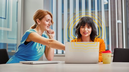 Two women working together on a laptop that is placed on the table in front of them.