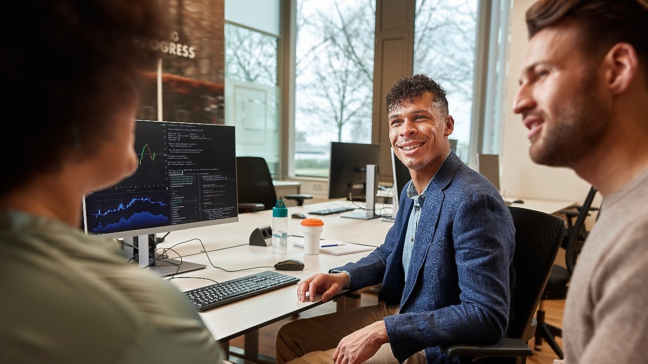 Three employees sitting and talking to each other at the workstation.