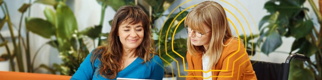 Two employees are seated and looking at an iPad, with one of them in a wheelchair