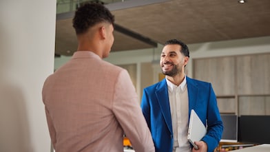 Two employees exchange smiles as they greet each other with a handshake.