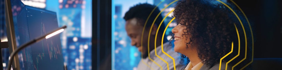 Women and men smiling and sitting in front of the computer screens. Behind them big windows with city view.​