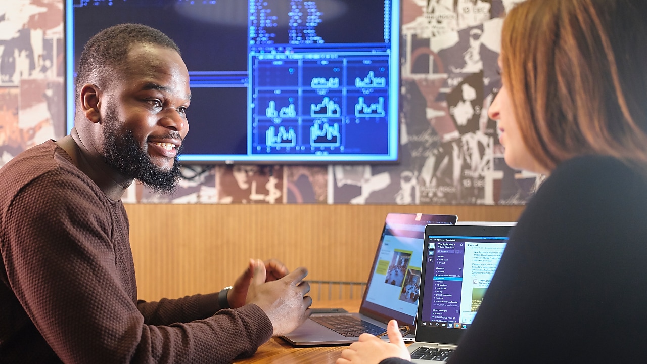 Two employees talking while using their computers