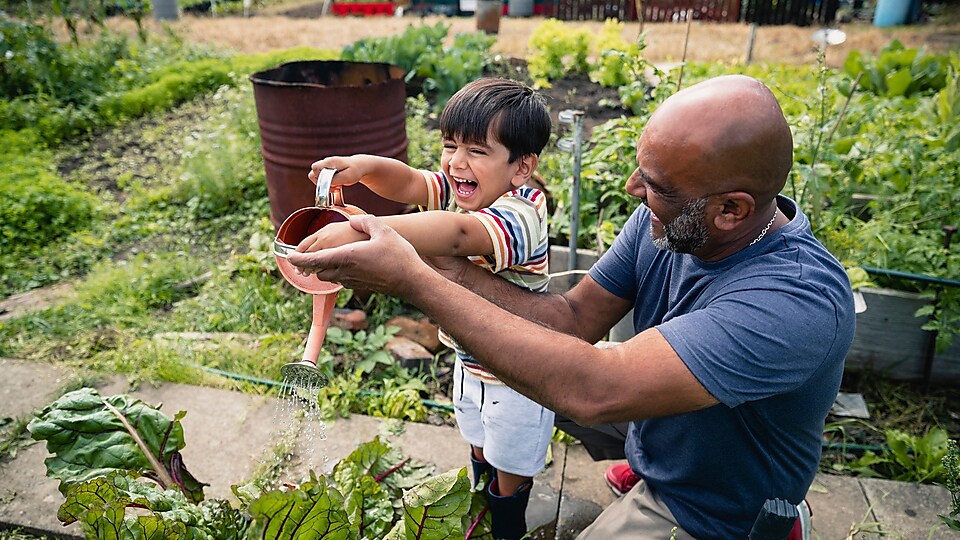 Mężczyzna pomagający uśmiechniętemu dziecku podlewać rośliny w ogrodzie