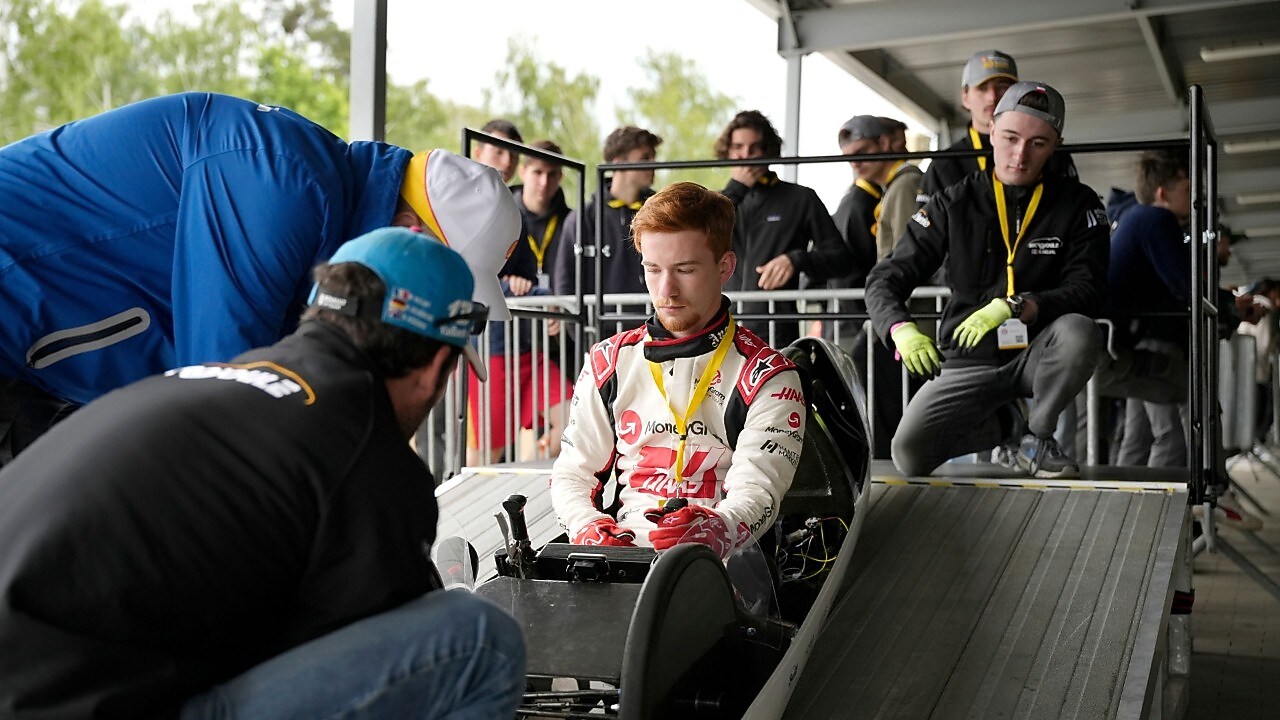 student siedzi w bolidzie a dwóch mechaników sprawdza pojazd