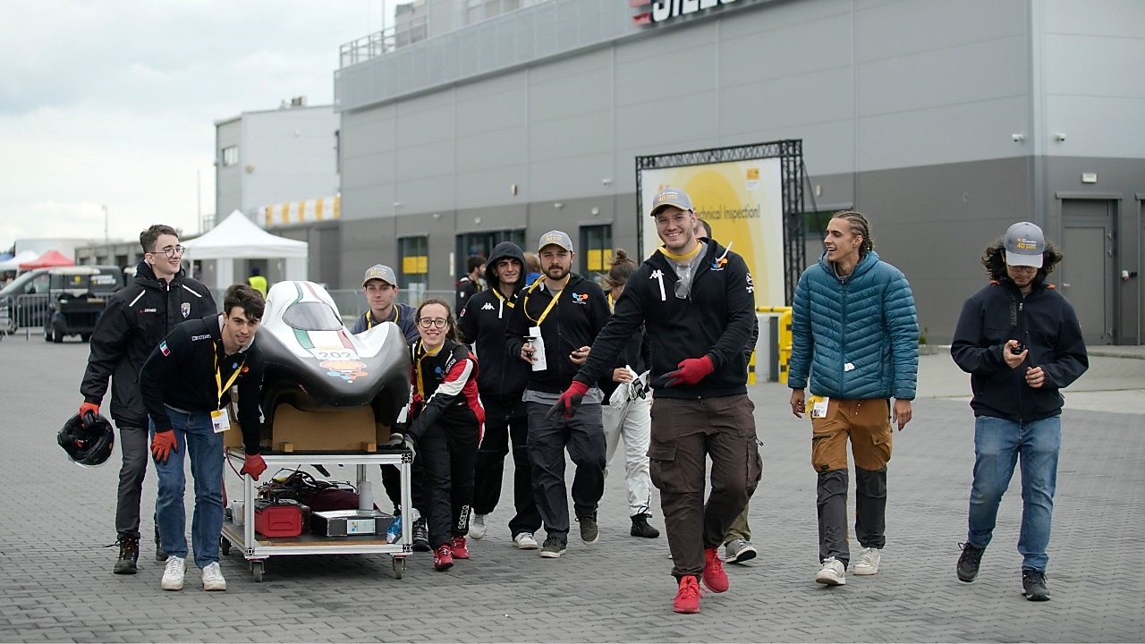 grupa studentów przesuwa bolid, który jest na wózku