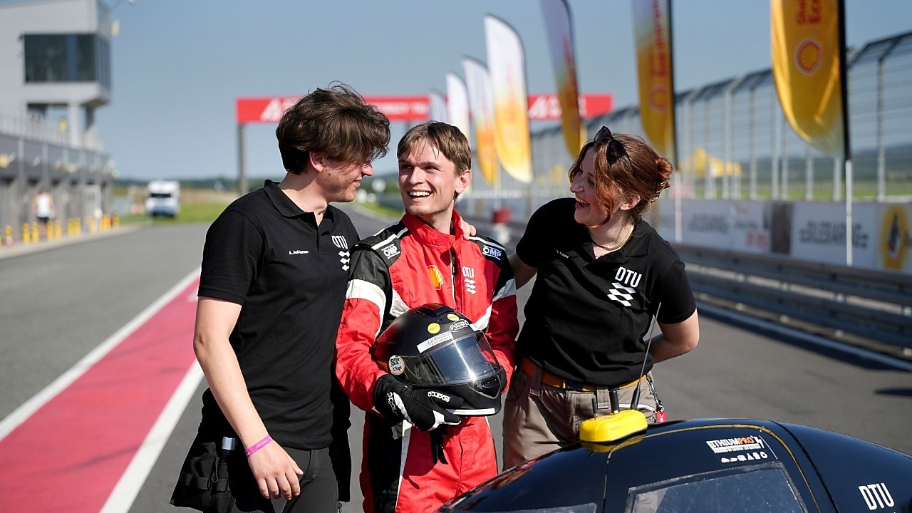 uśmiechnięta trójka studentów na tle flag Shell Eco-marathon