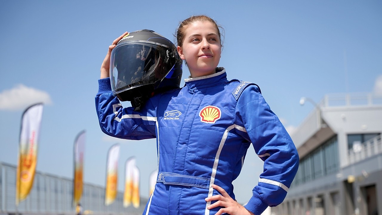 uśmiechnięta studentka w niebieskim kobinezonie wyścigowym i czarnym kasku trzymanym na ramieniu