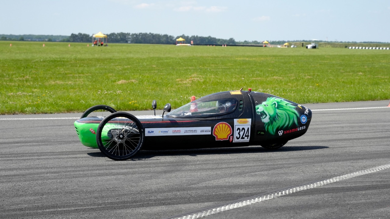 czarny bolid trzy kołowy z rusunkiem zielonego lwa poruszający się po torze