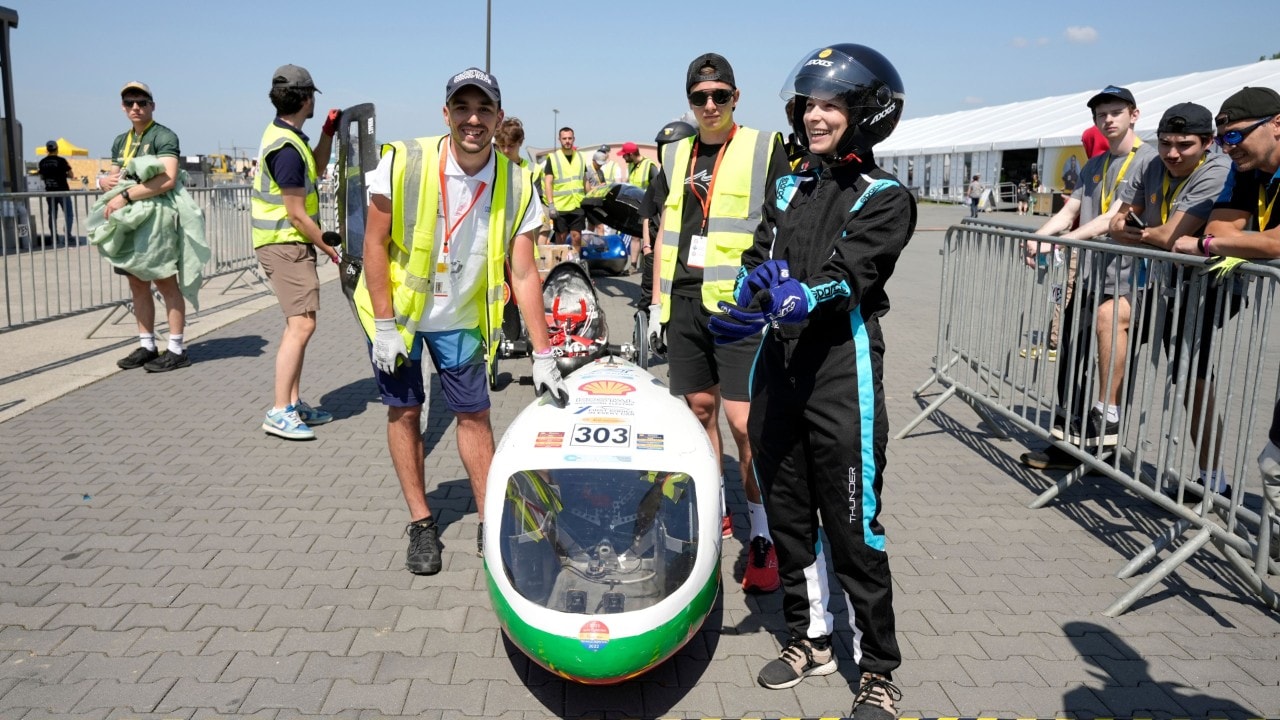 trójka studentów stojąca nad biało zielonym bolidem
