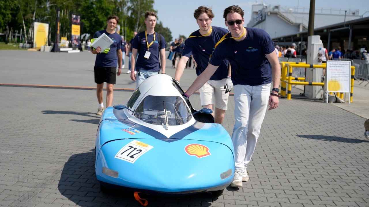 czterech studentów pchających niebieski bolid