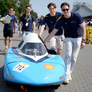 czterech studentów pchających niebieski bolid