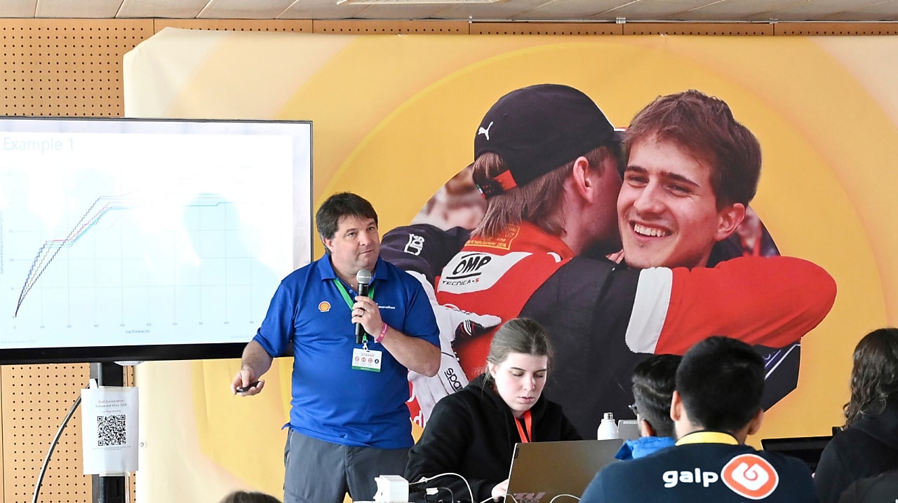 Person in blue holding a microphone, presenting a lecture to an audience of young people