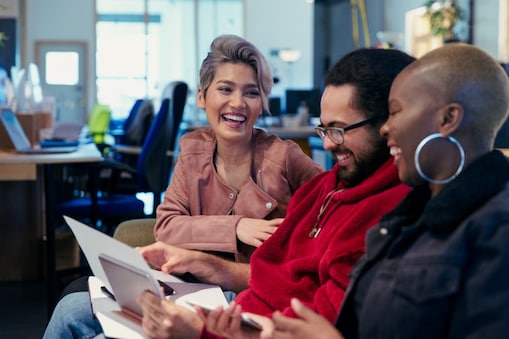 Trzy osoby w biurze siedzące razem, przeglądające dokumenty i śmiejące się