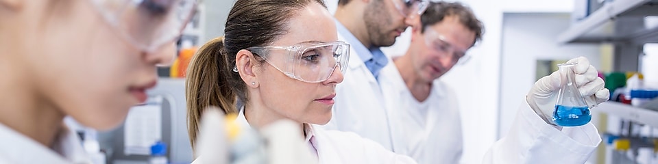Naukowcy w laboratorium w białych kitlach i okularach ochronnych zajmują się próbkami