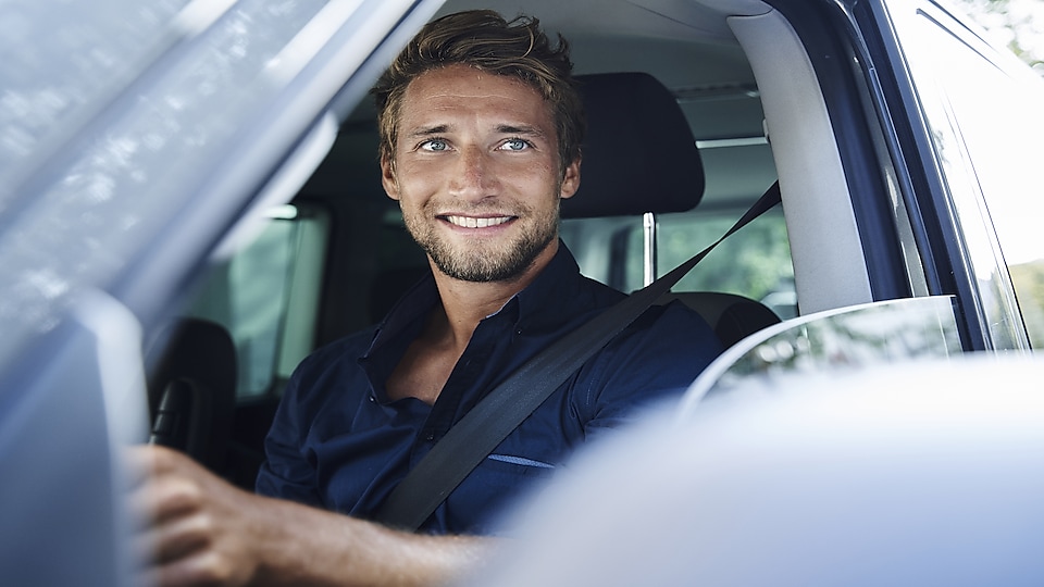 Odpowiednio zorganizowany harmonogram pracy kierowcy to zadowolony pracownik. Uśmiechnięty mężczyzna w samochodzie.