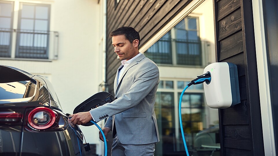 Mężczyzna ubrany w garnitur ładuje samochód elektryczny.
