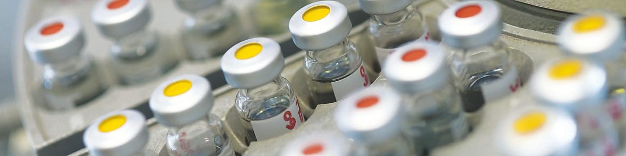 Rows of medicine vials sitting in a holder, some with red dots on the lid, and some with yellow dots on the lid