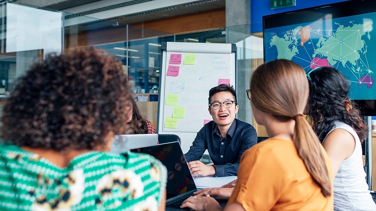 Four business people sitting around a round table reading documents, grey and yellow carpet