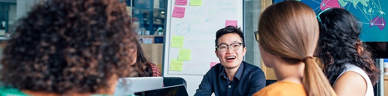 Four business people sitting around a round table reading documents, grey and yellow carpet