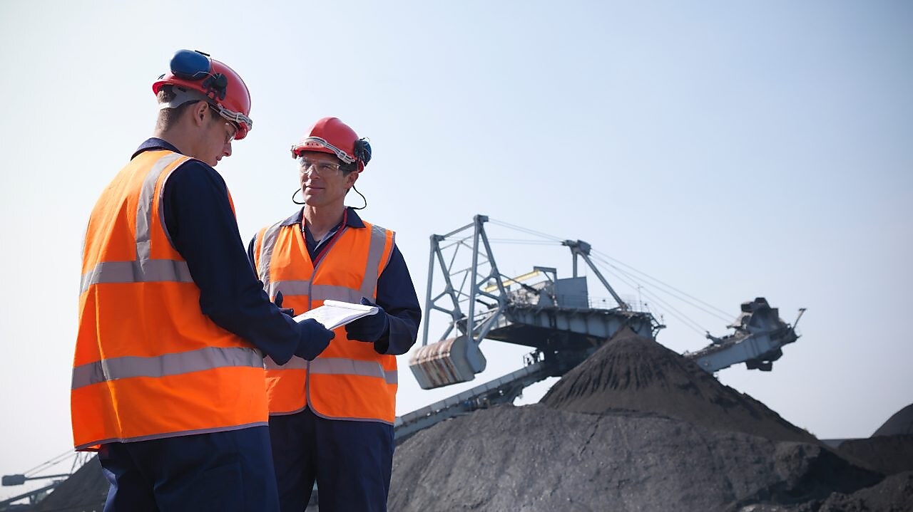 Dwóch pracowników w kamizelkach odblaskowych i kaskach ochronnych w kopalni
