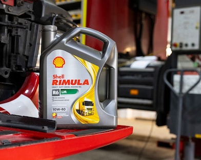 A bottle of Shell Rimula heavy-duty diesel engine oil placed on a red truck part inside a workshop.