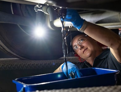A mechanic drains oil from a vehicle into a blue container in a workshop