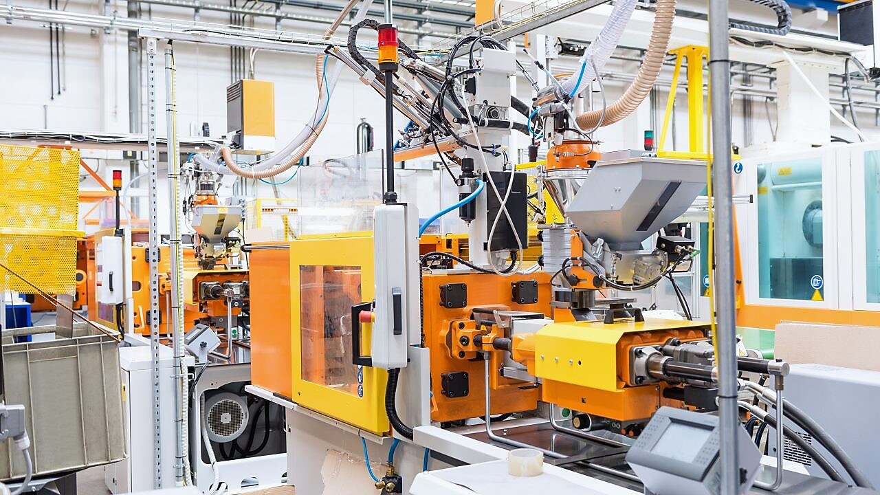 Horizontal color image of automated injection moulding machine working on plastic parts production. Powerful molding machinery in factory arranged in a row.