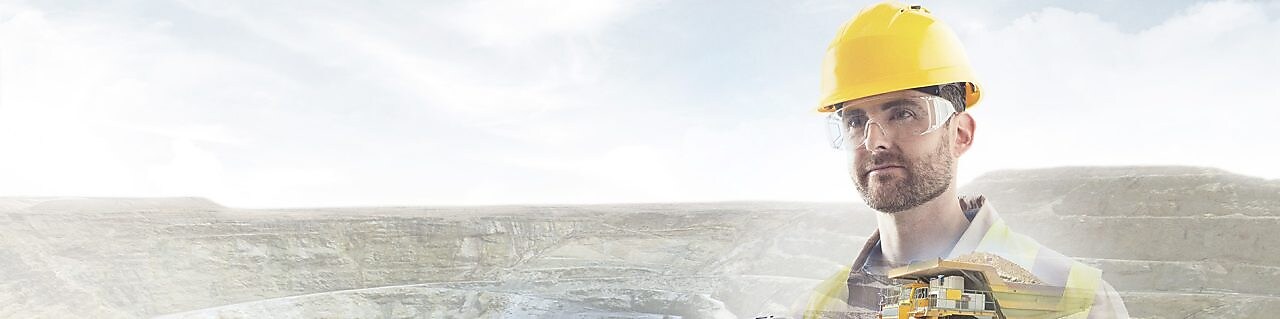 robotnik w żółtym kasku na tle klifów i duża żółta ciężarówka