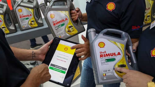 Trzy osoby trzymające butelki Shell Rimula oraz tablet wyświetlający Shell CO₂ and Energy Tracker. W tle znajdują się półki z kolejnymi butelkami Shell Rimula.