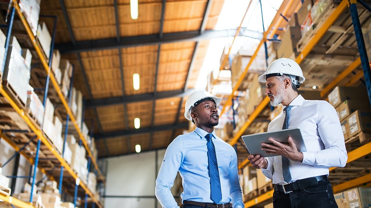 Kierownicy stoją w magazynie z tabletem, rozmawiają.