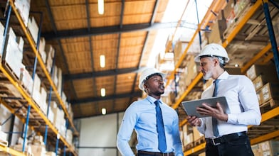 Kierownicy stoją w magazynie z tabletem, rozmawiają.