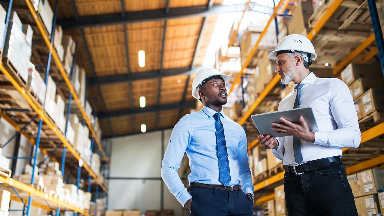 Kierownicy stoją w magazynie z tabletem, rozmawiają.