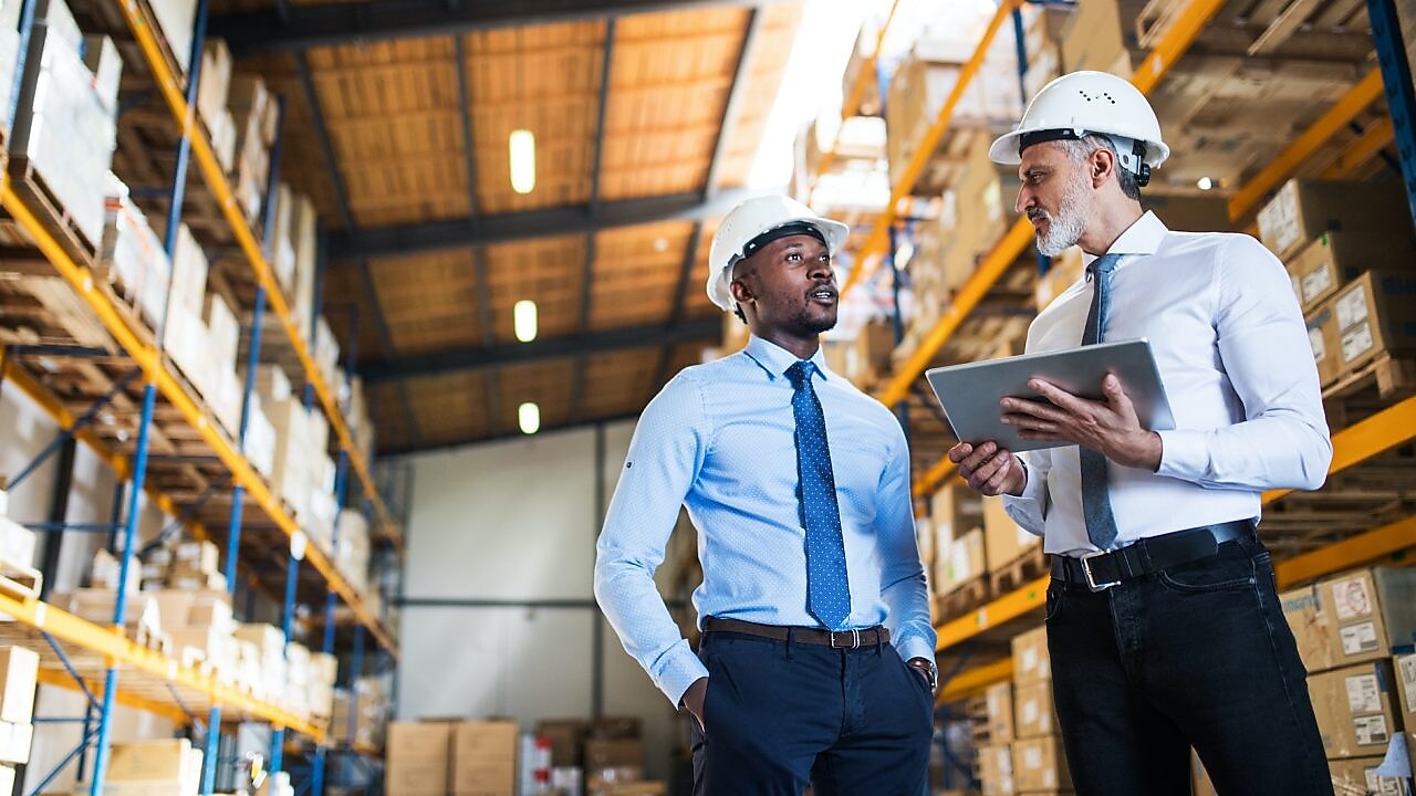 Kierownicy stoją w magazynie z tabletem, rozmawiają.