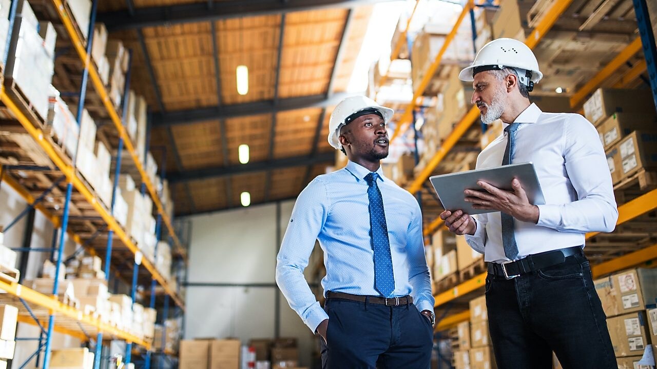 Kierownicy stoją w magazynie z tabletem, rozmawiają.