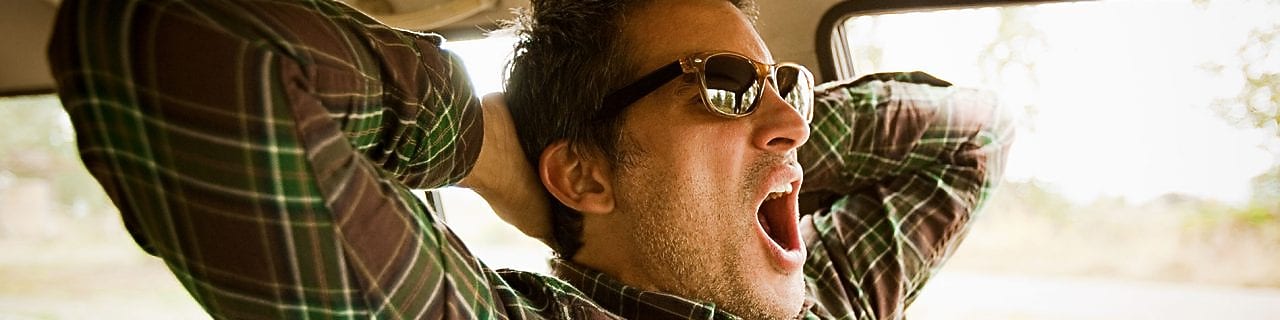 a man yawns in a car, indicating that he needs sleep