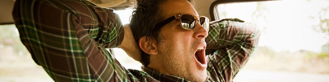 a man yawns in a car, indicating that he needs sleep