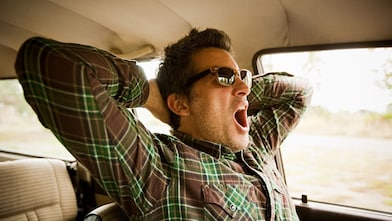 a man yawns in a car, indicating that he needs sleep