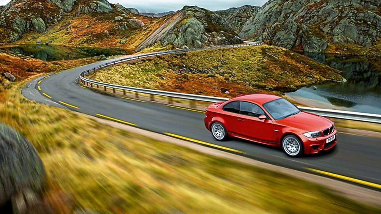 Czerwony sedan na wijącej się górskiej drodze w Norwegii