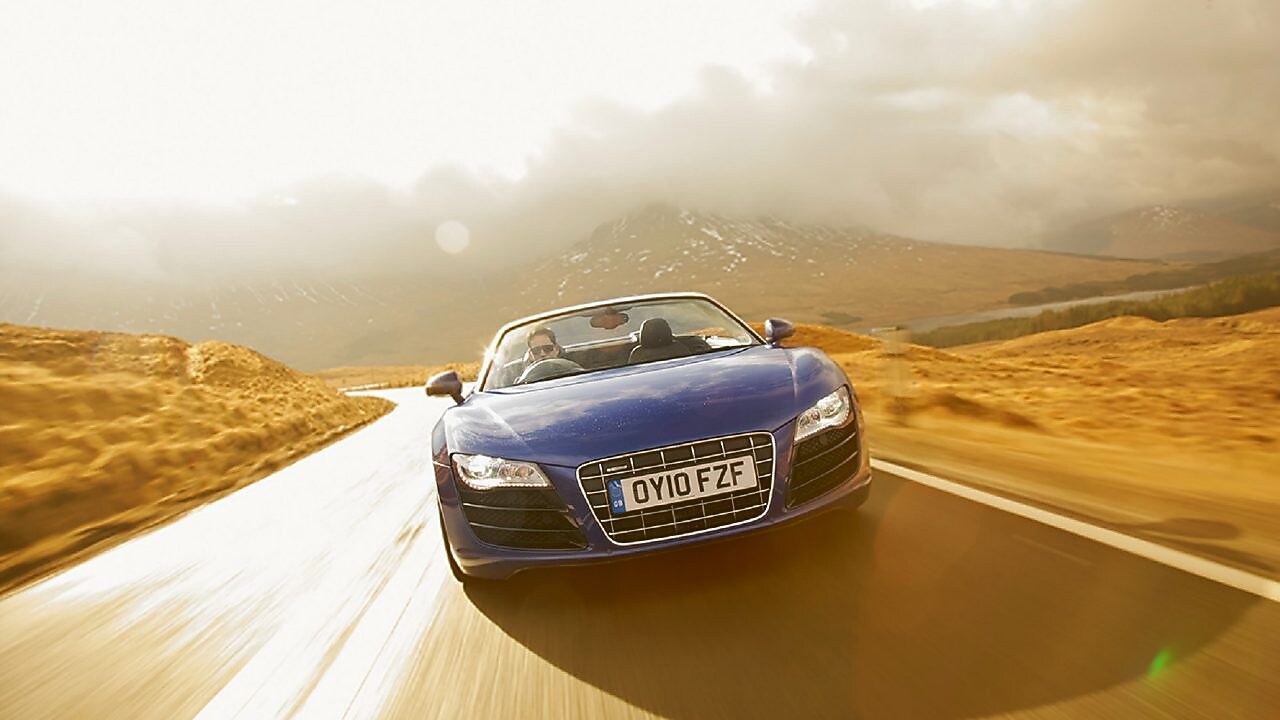 Niebieski kabriolet jadący przez tereny wiejskie w górskiej scenerii