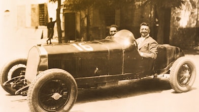 Czarno-białe zdjęcie Enzo Ferrari siedzącego w jednym z pierwszych samochodów Ferrari