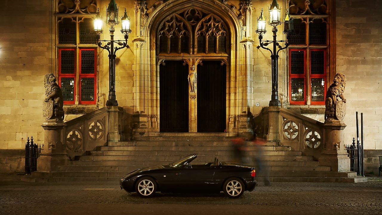 Czarny samochód zaparkowany nocą przed dużym domem obok kamiennych stopni