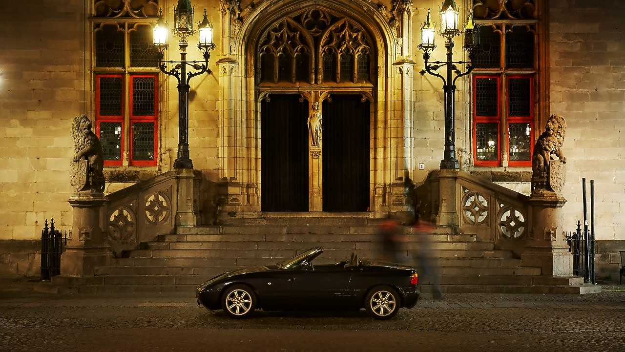 Czarny samochód zaparkowany nocą przed dużym domem obok kamiennych stopni