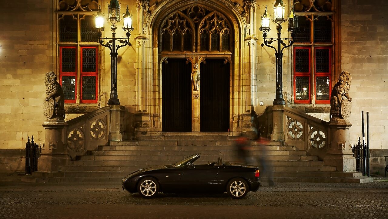 Czarny samochód zaparkowany nocą przed dużym domem obok kamiennych stopni