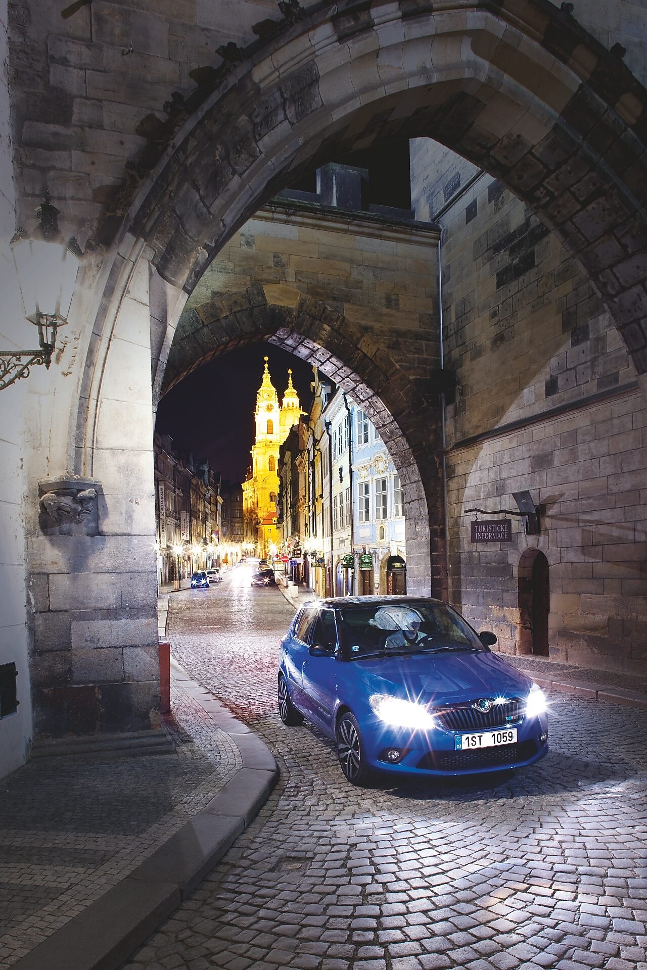 Niebieski samochód zaparkowany pod łukiem na brukowanej praskiej ulicy nocą