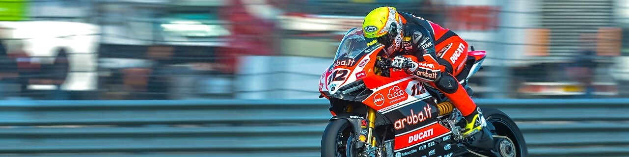 Superbike Ducati z zawodnikiem mknącym po torze wyścigowym, z ciężarówkami w tle