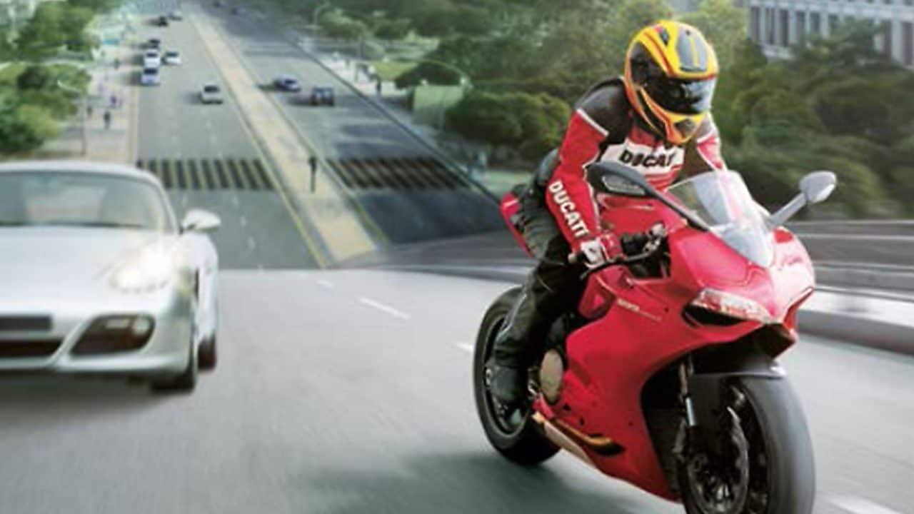 Czerwony motocykl i motocyklista na drodze między samochodami z budynkami w tle