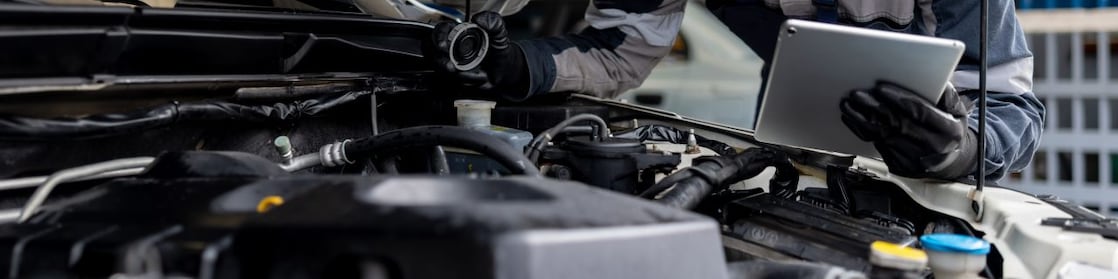 Male mechanic checking the levels of a liquid on a car using a tablet digital device in a garage auto repair shop.
