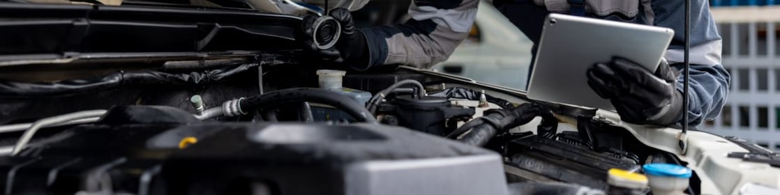 Male mechanic checking the levels of a liquid on a car using a tablet digital device in a garage auto repair shop.