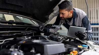 Male mechanic checking the levels of a liquid on a car using a tablet digital device in a garage auto repair shop.